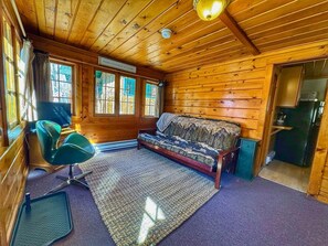 Ein gemütliches Blockhaus-Interieur mit Holzbalkendecke, einer Couch, einem Sessel und einer kleinen Küchenzeile.