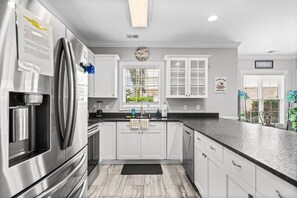 A modern kitchen with white cabinets, stainless steel appliances, a black countertop, and a window with blinds. - Magnolia Pointe Golf & Beach Retreat Myrtle Beach (Myrtle Beach)