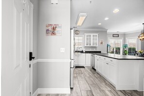 A modern kitchen with white cabinetry, a central island, and a clock on the wall. - Magnolia Pointe Golf & Beach Retreat Myrtle Beach (Myrtle Beach)