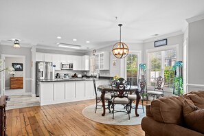 A modern kitchen with white cabinetry, a dining area with a round table and chairs, and a living room with a brown sofa. - Magnolia Pointe Golf & Beach Retreat Myrtle Beach (Myrtle Beach)