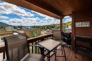 A covered outdoor deck with a table and chairs, overlooking a lake and buildings. - Walk to town, natural lake and MTN view, balcony (Grand Lake)