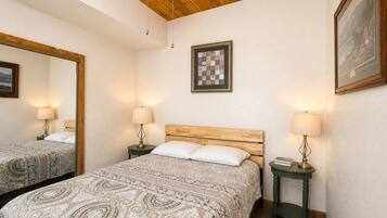 A bedroom with two beds, a wooden ceiling, a framed artwork, and bedside lamps.