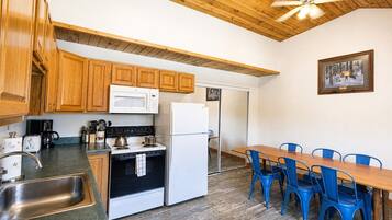 A compact kitchen with wooden cabinets, a microwave, stove, refrigerator, and a dining area with blue chairs.