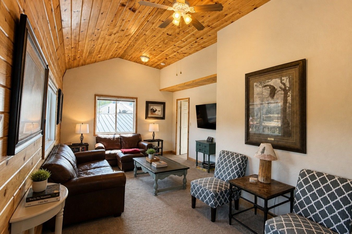 A cozy living room with a wooden ceiling, leather sofas, a coffee table, and a television.