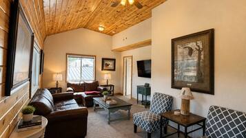 A cozy living room with a wooden ceiling, leather sofas, a coffee table, and a television.