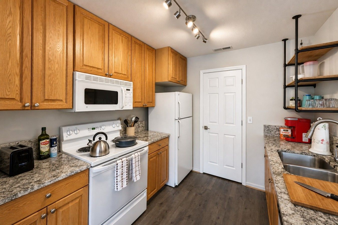 A kitchen with wooden cabinets, a white microwave, a stove, a refrigerator, and a granite countertop.