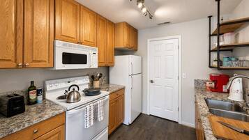 A kitchen with wooden cabinets, a white microwave, a stove, a refrigerator, and a granite countertop.
