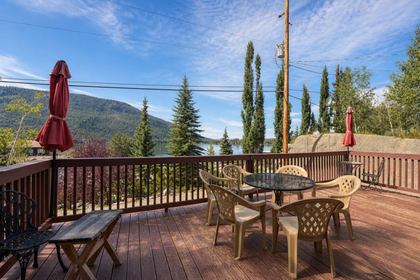 A deck with outdoor furniture, a view of a lake, and a forested mountain backdrop.
