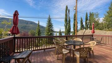 A deck with outdoor furniture, a view of a lake, and a forested mountain backdrop.
