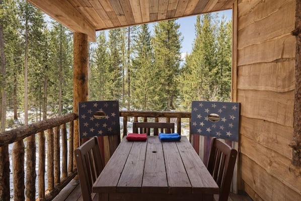Een houten terras met een tafel en stoelen, omringd door een houten balustrade, met uitzicht op een bos.