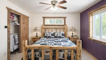 A bedroom with a wooden bed, two bedside tables with lamps, a ceiling fan, a window with a view of trees, and a closet with hanging clothes.