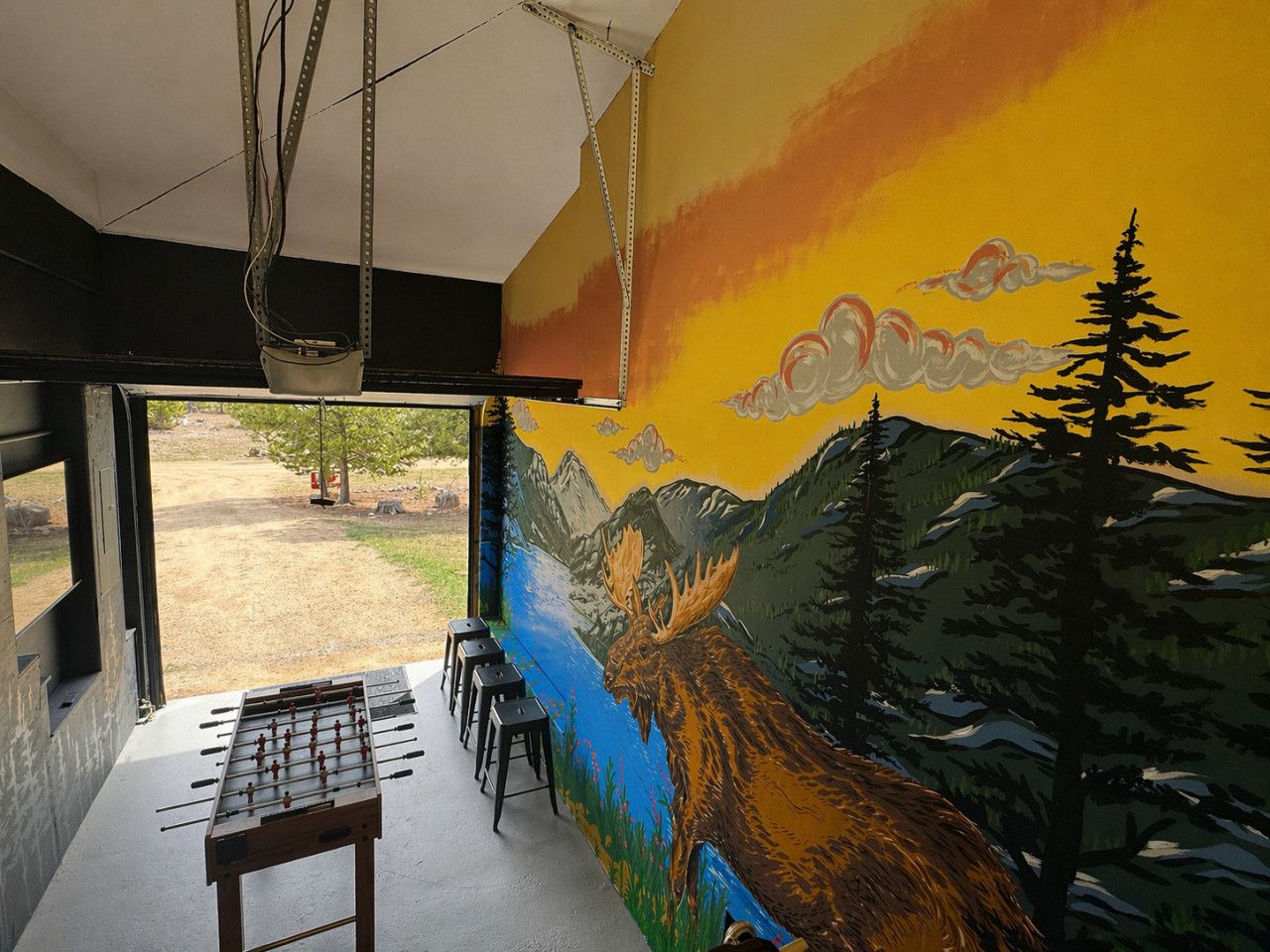 A room with a mural of a mountain landscape, a foosball table, and bar stools.