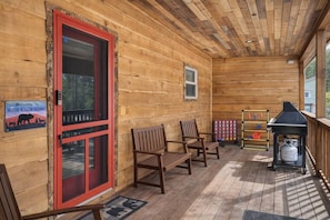 Uma cabana de madeira com porta vermelha, um banco, churrasqueira e uma placa de boas-vindas ao Moose Hollow Hideaway.