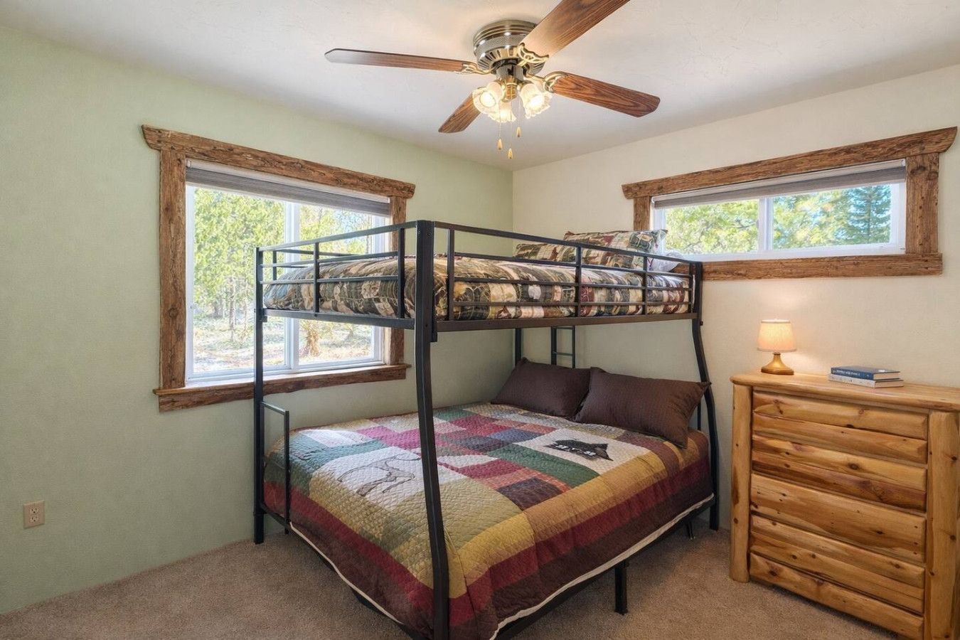 A bunk bed with a quilt, a wooden dresser, and a ceiling fan in a room with windows.