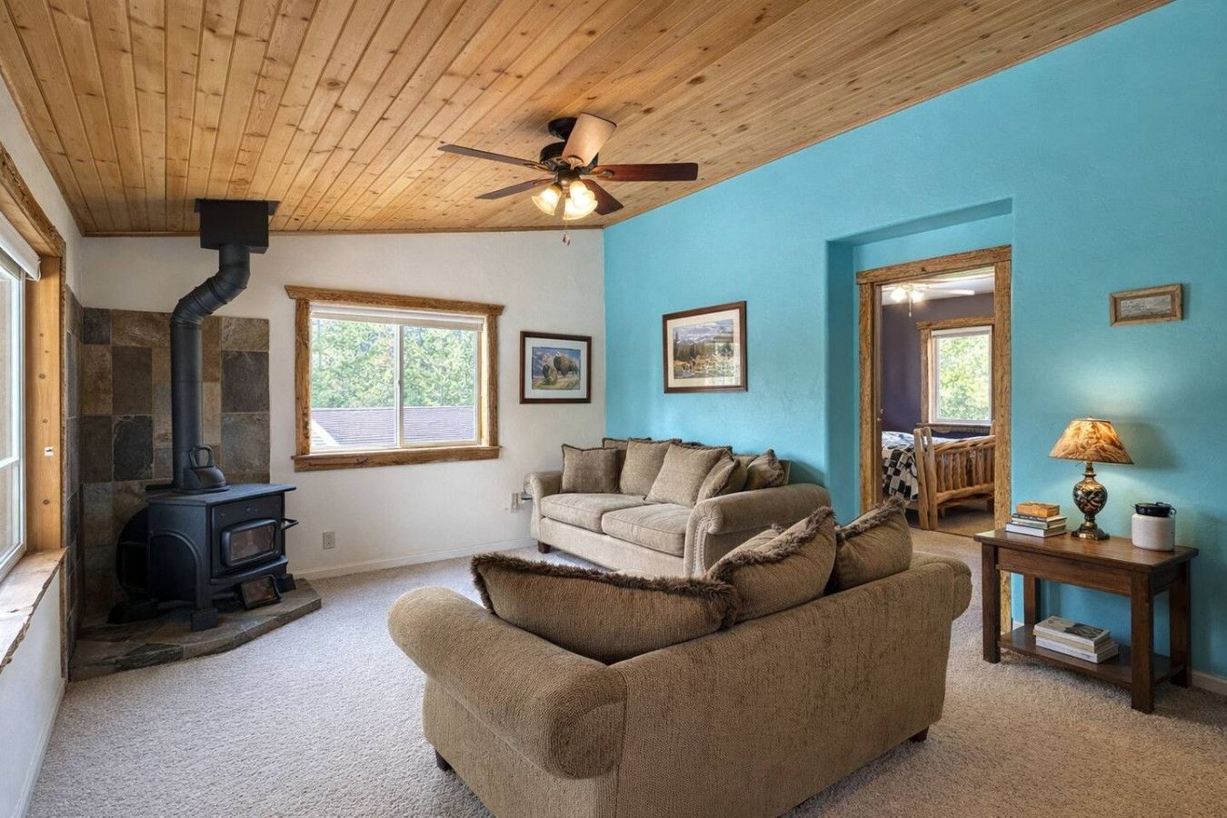 A cozy living room with a stone fireplace, a sofa, a ceiling fan, and a window.