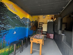Een tafelvoetbaltafel in een kamer met een muurschildering van een berglandschap en een zeilboot.