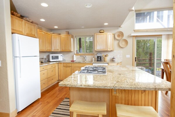 A kitchen with wooden cabinets, a white refrigerator, a microwave, a stove, and a large island with stools.
