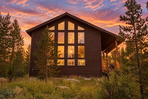 A wooden cabin with large windows, surrounded by trees and a grassy area. - Glacial boulder cabin with panoramic mountain view (Grand Lake)