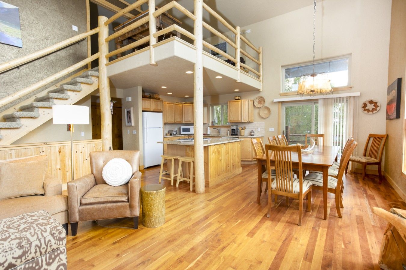 Amplia sala de estar con una escalera de madera, una mesa de comedor con sillas y una zona de cocina.
