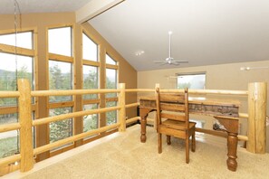 Una habitación con un escritorio de madera, una silla y un amplio ventanal con vistas a árboles.