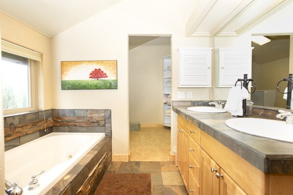 A bathroom with a large bathtub, two sinks, wooden cabinets, and a painting on the wall. - Glacial boulder cabin with panoramic mountain view (Grand Lake)
