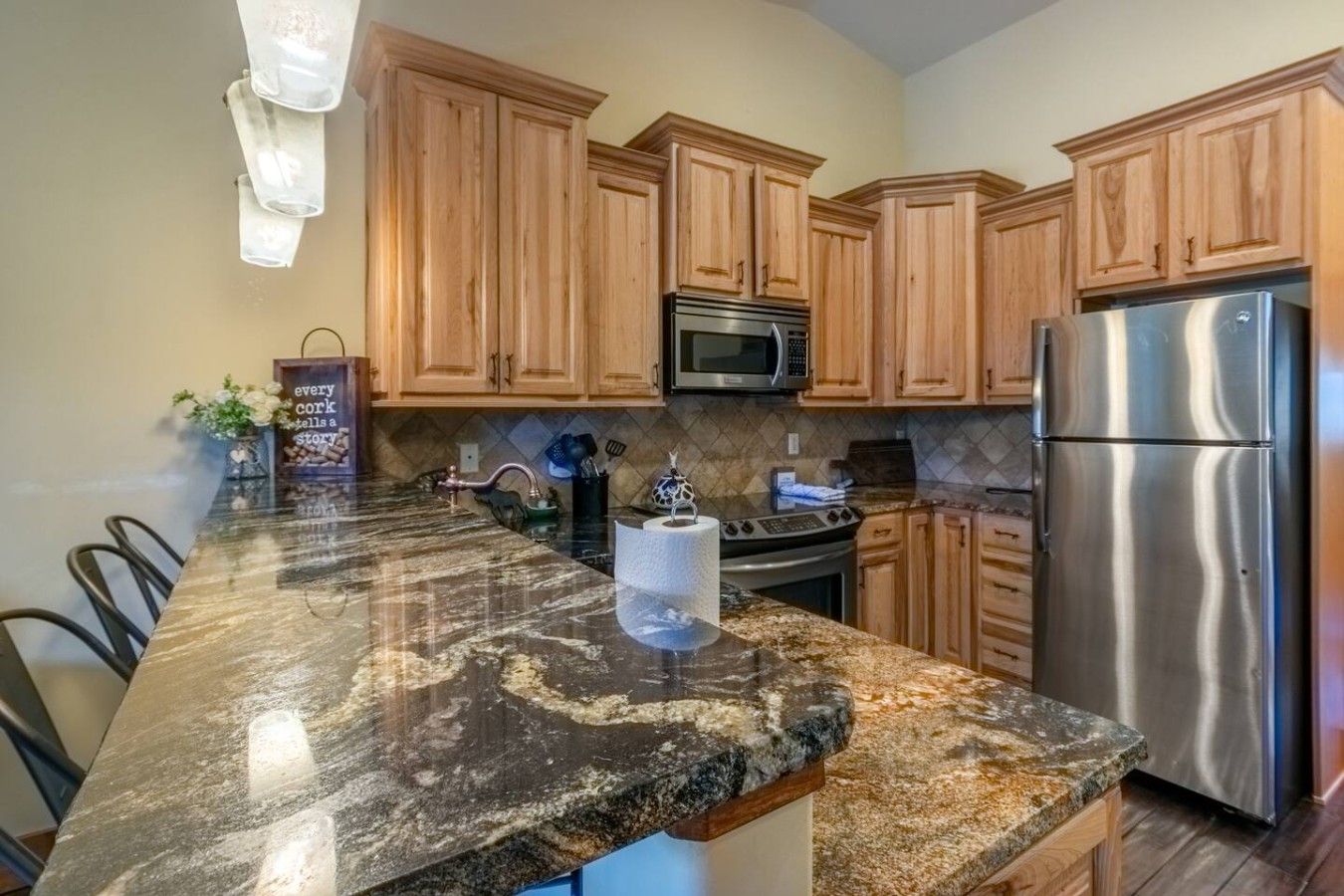 A kitchen with granite countertops, wooden cabinets, stainless steel appliances, and a marble backsplash.