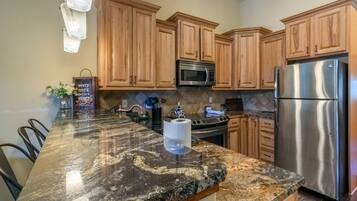A kitchen with granite countertops, wooden cabinets, stainless steel appliances, and a marble backsplash.