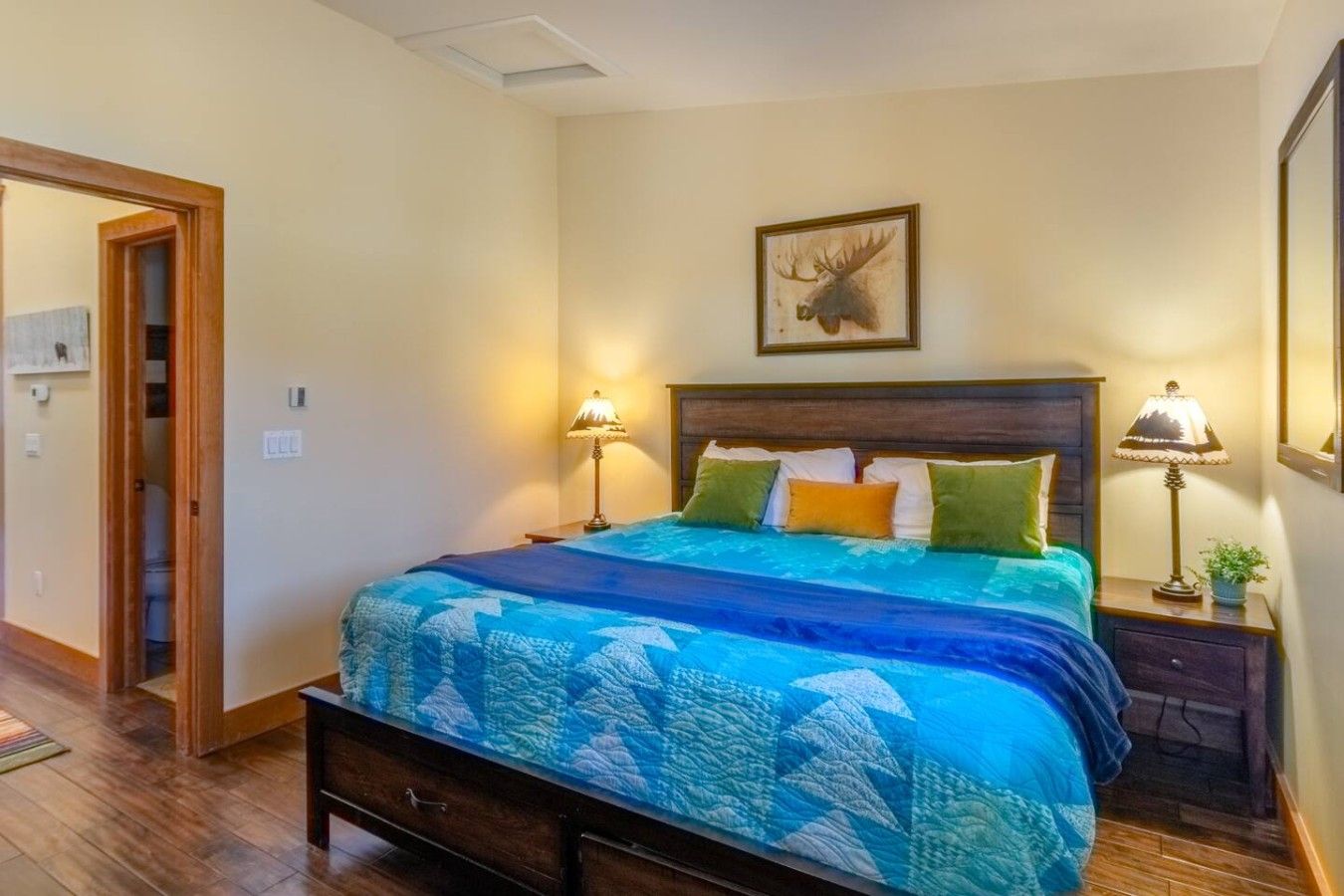 Un dormitorio con cama, dos lámparas de noche, un cuadro enmarcado en la pared y una puerta de madera.