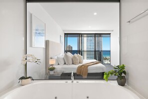 A modern bedroom with a large bed, a bathtub, and a view of the cityscape. - Circle on Cavill Ocean View (Surfers Paradise)