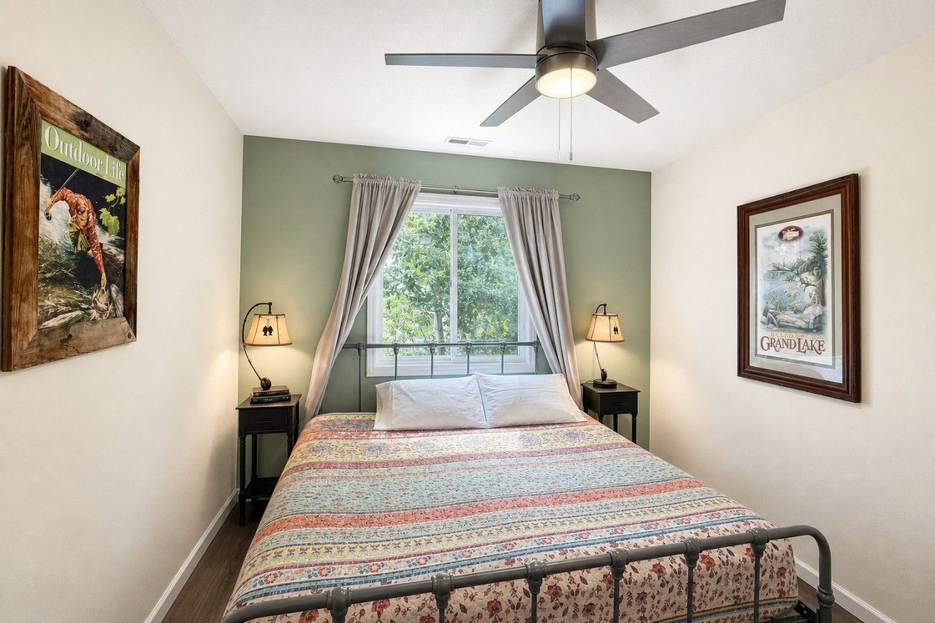 A bedroom with a bed, two bedside lamps, a ceiling fan, and a window with curtains.