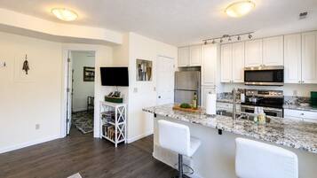 A modern kitchen with white cabinets, a granite countertop, stainless steel appliances, and a bar area with white stools.
