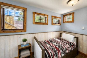 Ein Schlafzimmer mit einem Bett, einem Fenster, einer kleinen Ablage mit einer Pflanze und einer Deckenleuchte.