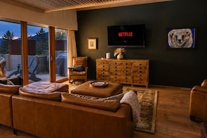 A living room with a leather sofa, wooden cabinet, and a television displaying 'NETFLIX'. - Downtown luxury retreat, Lake and MTN views, Yoga (Grand Lake)