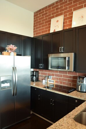 A kitchen with dark cabinets, a stainless steel refrigerator, a microwave, and a coffee station. - Uptown Condo | Skyline Views + Walkable Third Ward (Charlotte)