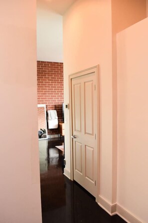 A hallway with a white door, a brick wall, and a coat rack. - Uptown Condo | Skyline Views + Walkable Third Ward (Charlotte)