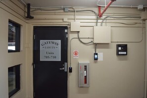 A door labeled 'GATEWAY LOFTS Units 705-710' with a 'NO EXIT' sign, electrical boxes, and a fire alarm on a beige wall. - Uptown Condo | Skyline Views + Walkable Third Ward (Charlotte)