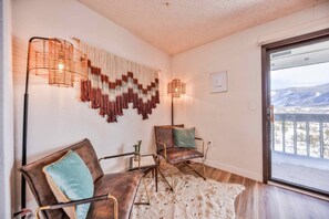 A modern living room with a sofa, chairs, a rug, and a large window with a mountain view.