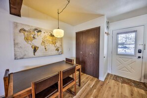 A dining area with a wooden table and chairs, a world map artwork on the wall, a wooden door, and a window with a view. - Epic Views of Grand Lake | Minutes to RMNP (Grand Lake)