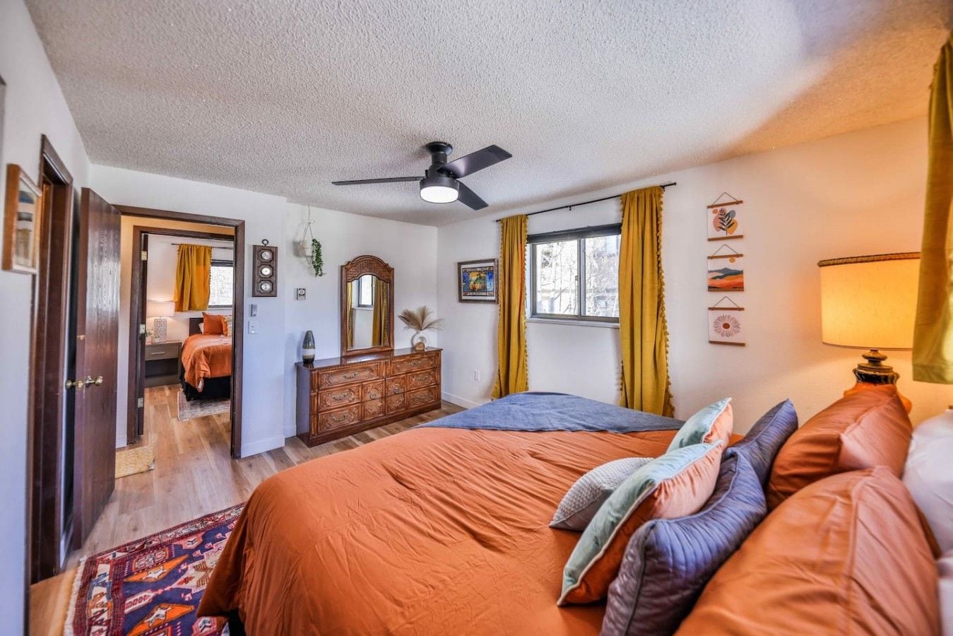 A bedroom with a bed, dresser, ceiling fan, and a view of another room.