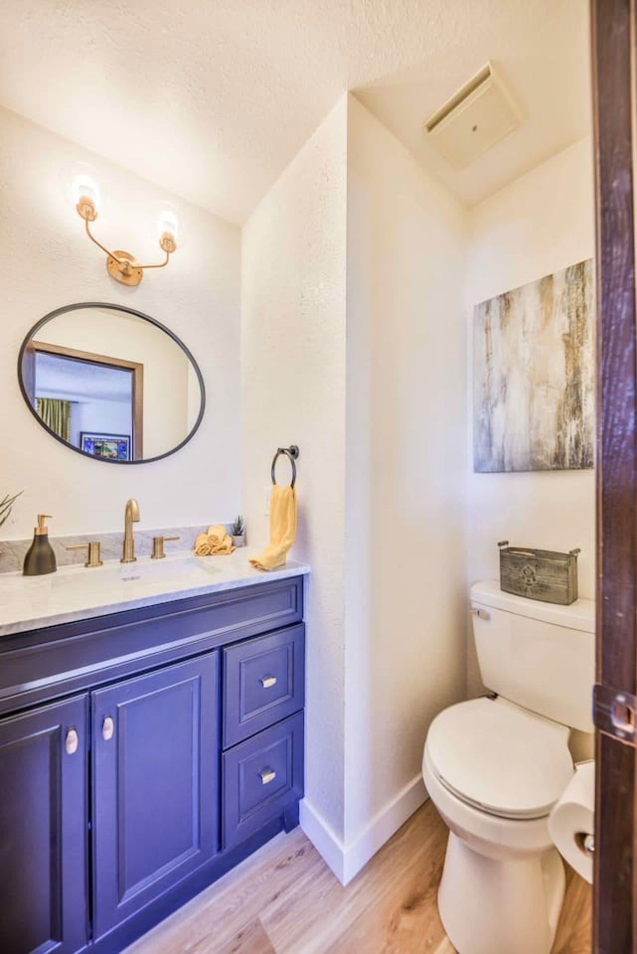 A bathroom with a white toilet, a dark blue vanity with a mirror, and a light-colored floor.