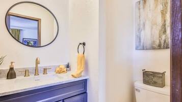 A bathroom with a white toilet, a dark blue vanity with a mirror, and a light-colored floor.