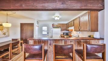 A kitchen with wooden cabinets, a central island with bar stools, and a dining area with a wooden table and chairs.
