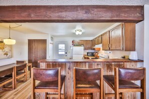 A kitchen with wooden cabinets, a central island with bar stools, and a dining area with a wooden table and chairs. - Epic Views of Grand Lake | Minutes to RMNP (Grand Lake)