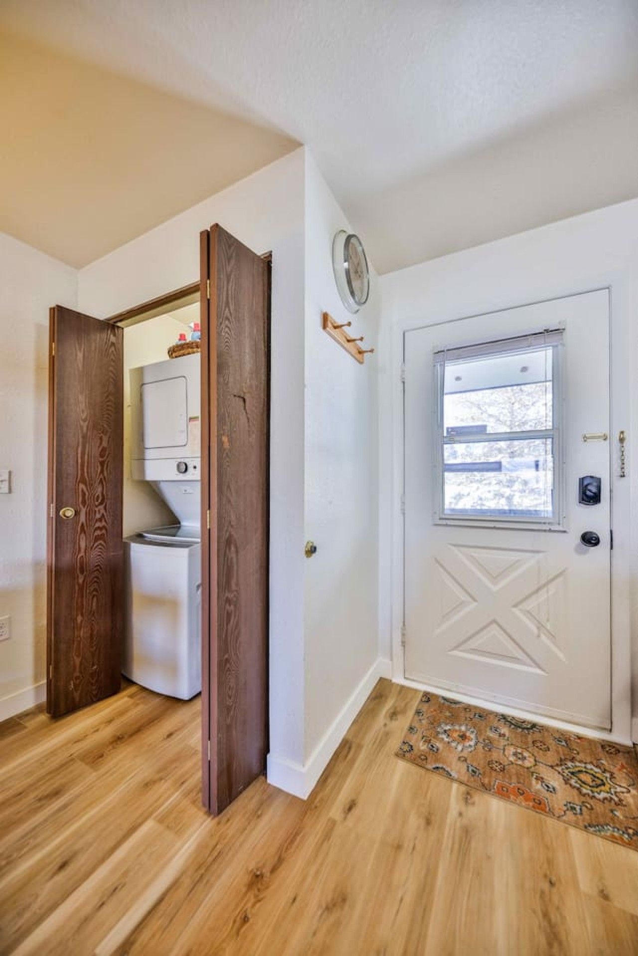 Un couloir avec une porte en bois donnant sur une buanderie, une porte blanche avec une fenêtre et un tapis à motifs sur le sol.