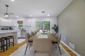 A modern kitchen with white cabinets, a dining area with a wooden table and chairs, and a view of greenery outside. - Your Poconos Escape | Game Room • Firepit • Grill (Tobyhanna)