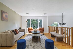 Ein geräumiges Wohnzimmer mit einer Couch, zwei Sesseln, einem Couchtisch und einer Treppe mit Geländer.