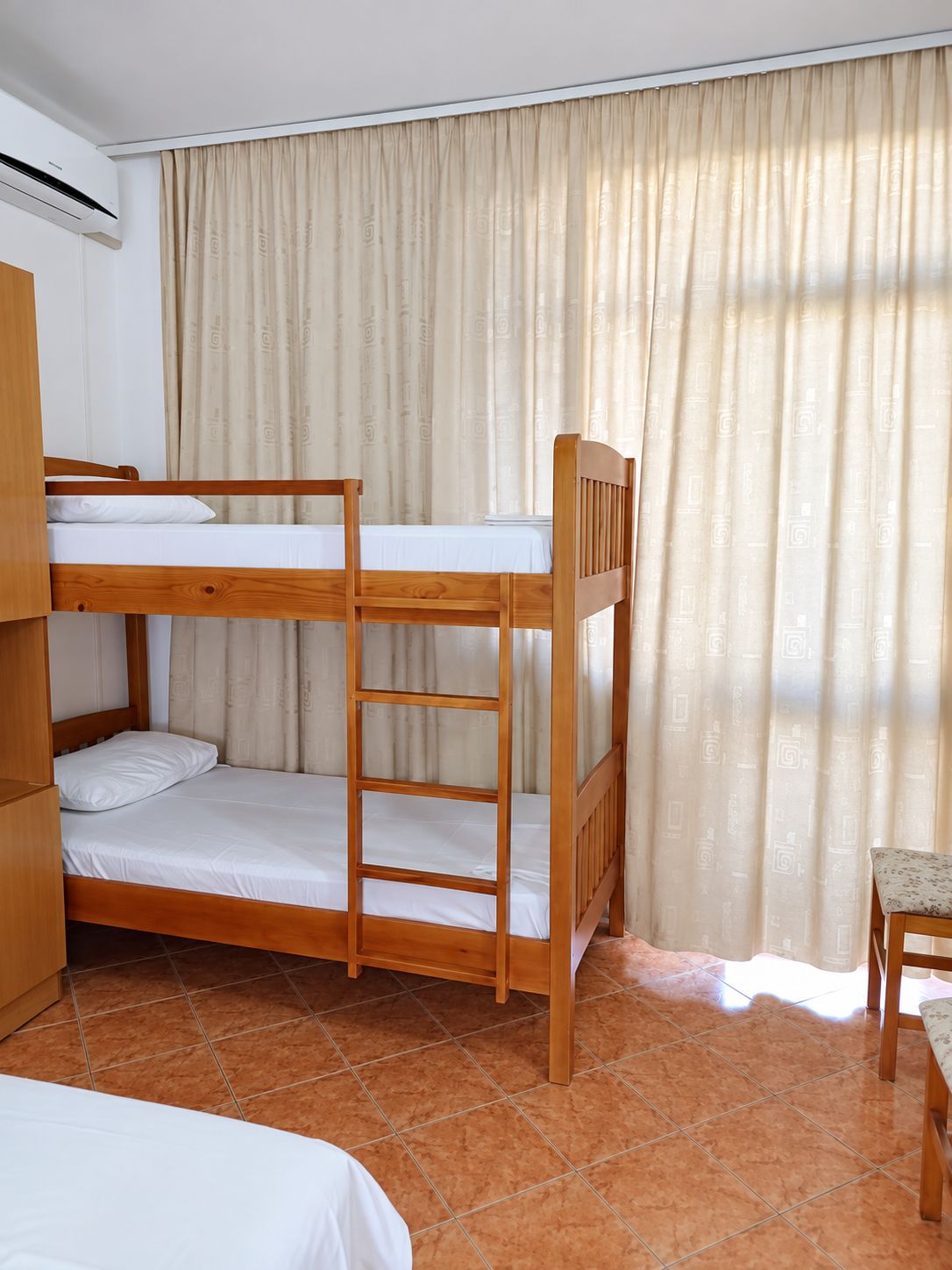 Ein Schlafzimmer mit Etagenbetten, einem hölzernen Kopfteil, einem kleinen Tisch und einem Vorhang.