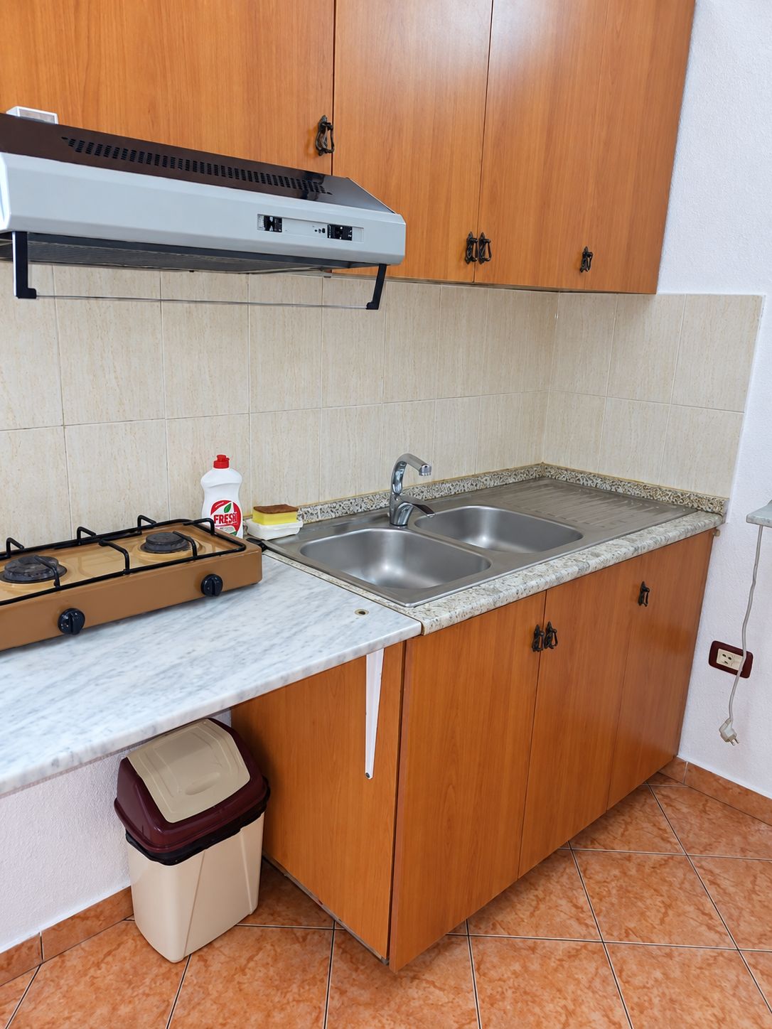 Una cocina con armarios de madera, estufa a gas, lavamanos y salpicadero de azulejos.