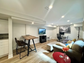 Ein modernes Wohnzimmer mit Essbereich, einem flachbildfernseher an der Wand und einem roten Akzenttisch.