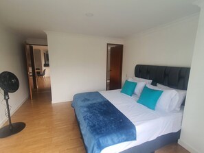 A bedroom with a bed, a standing fan, and a door leading to a bathroom. - Charming 2-bedroom Apartment in Medellín's Golden Mile (Medellín)